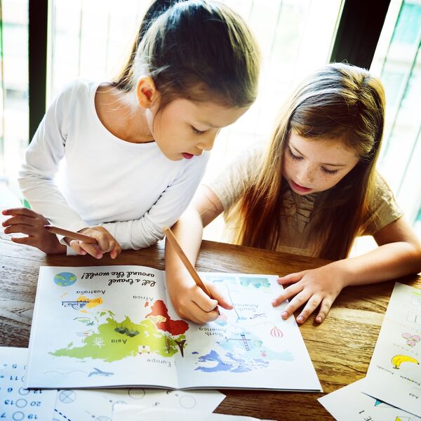 Due bambine che scrivono e colorano insieme su un quaderno