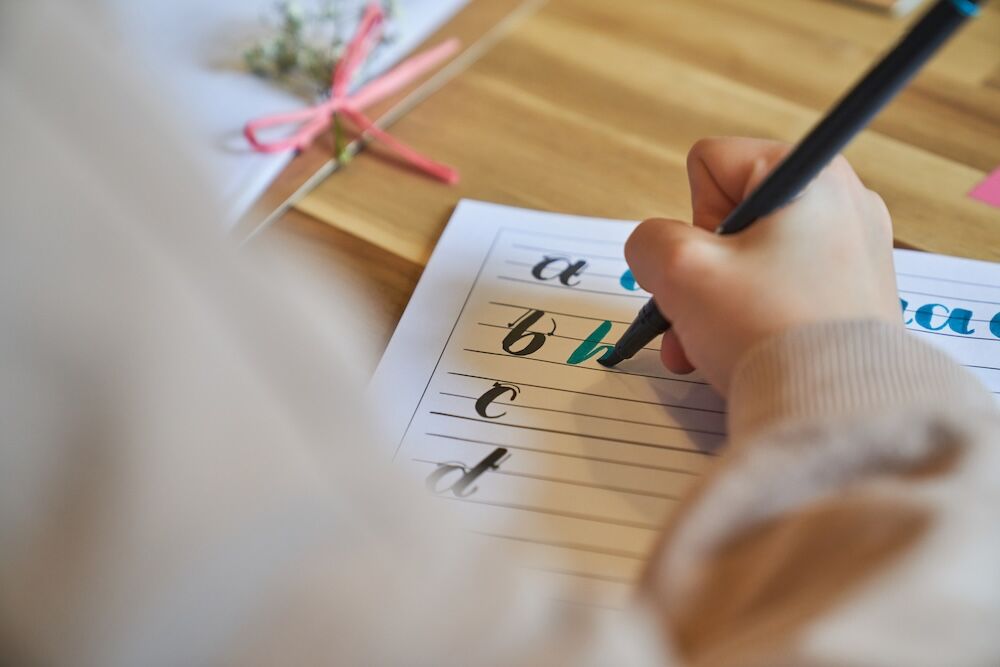 Mano di una bambina che ricalca lettere in corsivo su un quaderno