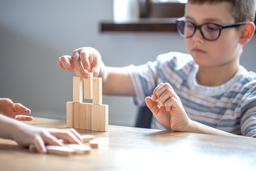 Bambino con gli occhiali che costruisce una torre di blocchi di legno