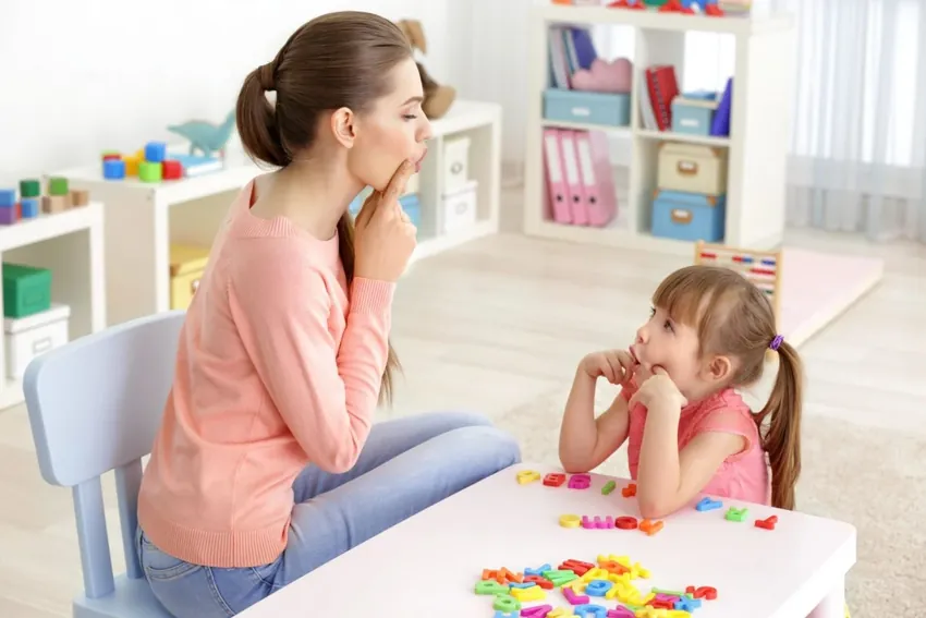 Logopedista e bambina al tavolino, con le lettere colorate dell'alfabeto